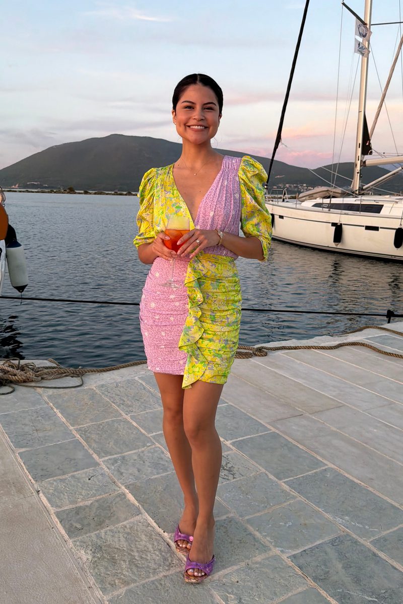Andrea Gabriela smiling on a harbor dock at sunset, wearing a pink and yellow floral dress